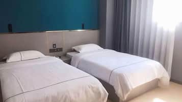 Habitación de hotel con dos camas, una pared de acento azul y un ventanal con cortinas.