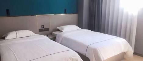 Habitación de hotel con dos camas, una pared de acento azul y un ventanal con cortinas.