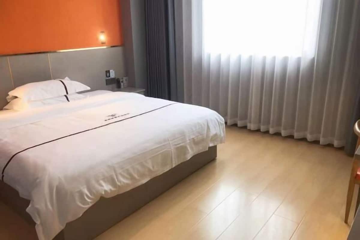 A hotel room with a bed, a nightstand, a lamp, and a window with curtains.