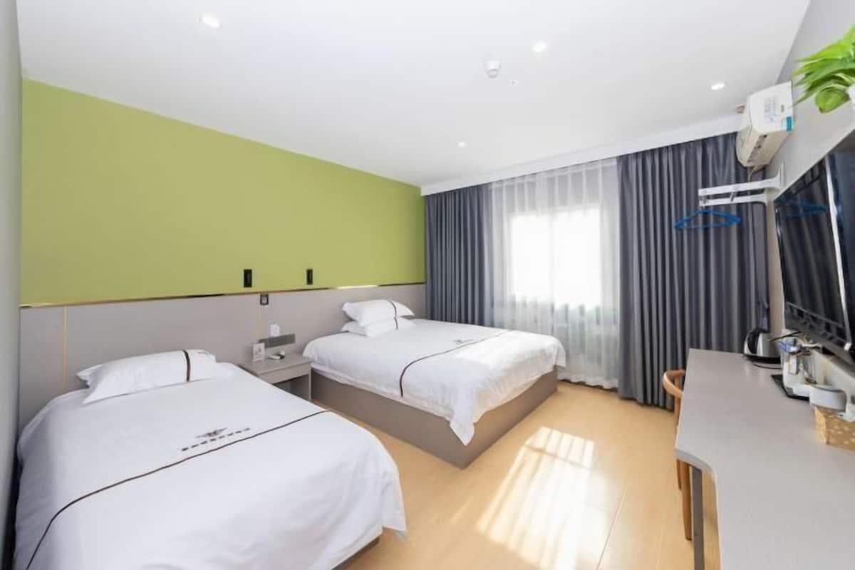 A hotel room with two beds, a desk, a chair, a mirror, and a window with curtains.