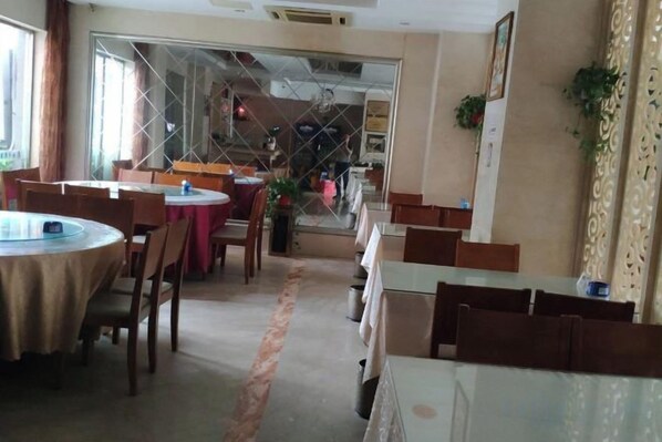Un comedor con mesas y sillas redondas, una cocina al fondo y vistas a través de un ventanal.