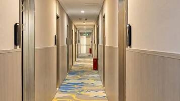 Un couloir d’hôtel avec des portes des deux côtés, une moquette à motifs et une poubelle rouge au centre.