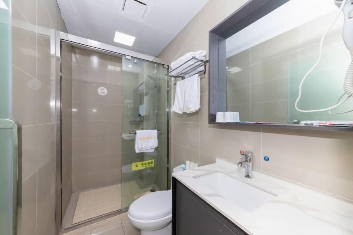 Uma casa de banho moderna com chuveiro em cabine de vidro, sanita branca, lavatório com espelho e um porta-toalhas.