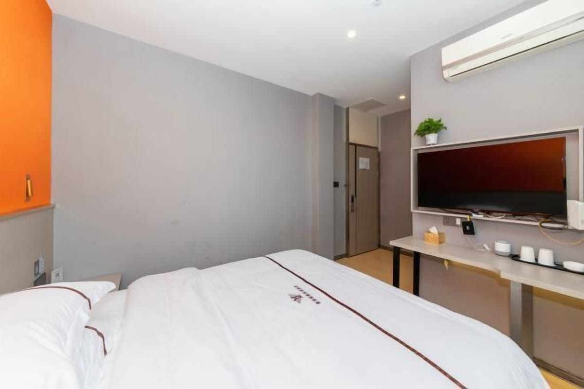 Quarto de hotel com cama, televisão na parede, uma mesinha com chávenas e um aparelho de ar condicionado.