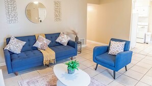 Ein Wohnzimmer mit blauem Sofa, blauem Sessel, einem runden Spiegel und Wanddekoration.