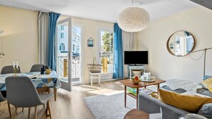 Un salon moderne comprenant un coin repas, un téléviseur et un balcon agrémenté de rideaux bleus.