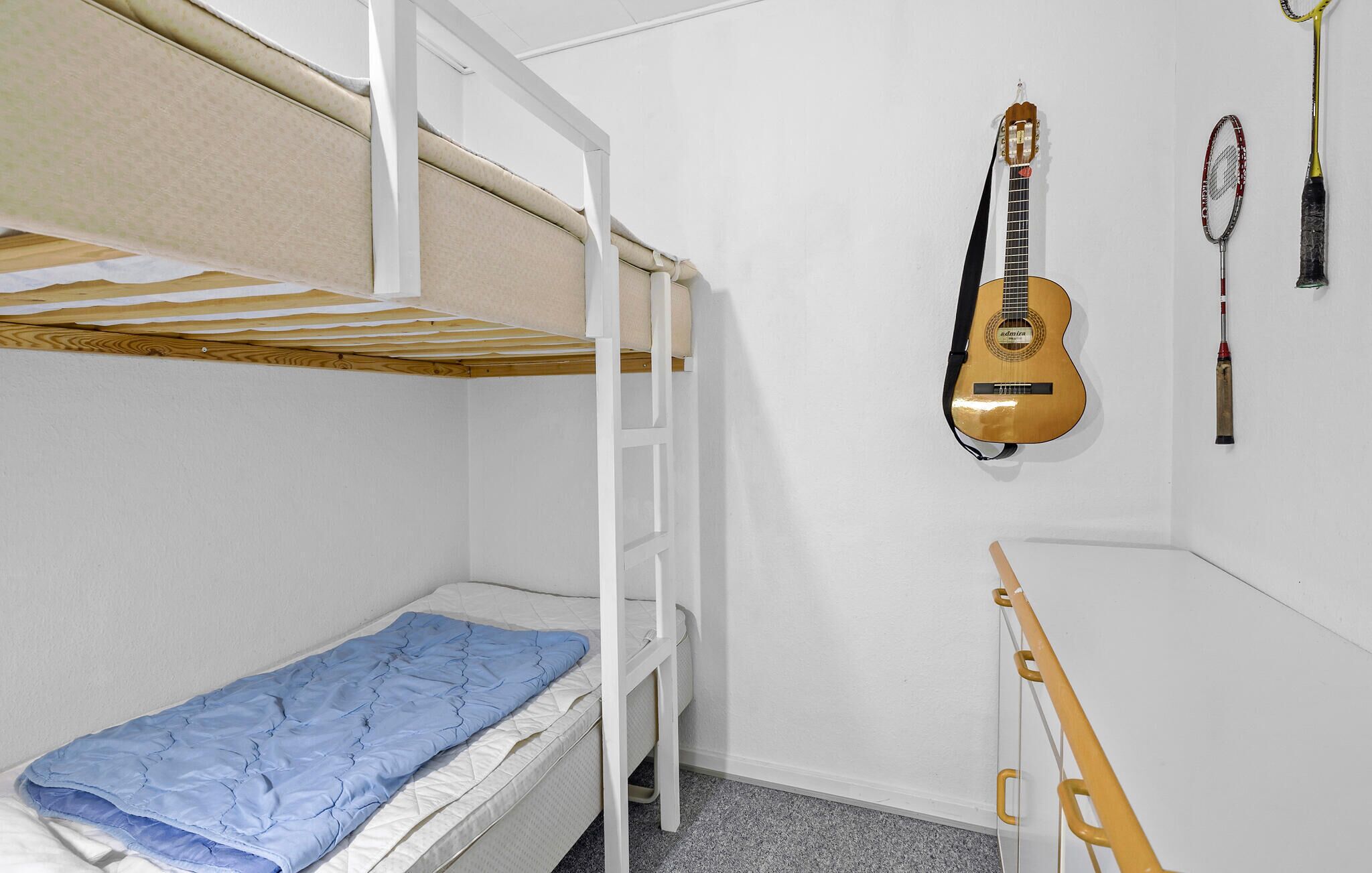 Habitació amb literes, una guitarra i una raqueta de tenis a la paret.
