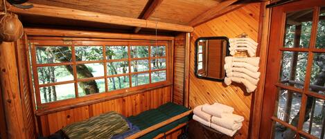 Ein Zimmer in einer Holzhütte mit einem Bett, einem Fenster mit Blick auf Bäume und einem Handtuchhalter mit Handtüchern.