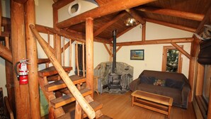 A rustic cabin interior with a stone fireplace, wooden staircase, and a cozy seating area. - Out 'N' About Treehouse Treesort (Cave Junction)
