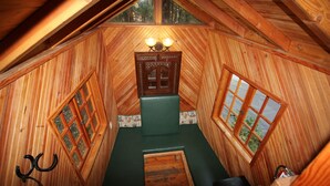 A wooden cabin with a loft bed, a small table, and a window with a view of trees. - Out 'N' About Treehouse Treesort (Cave Junction)