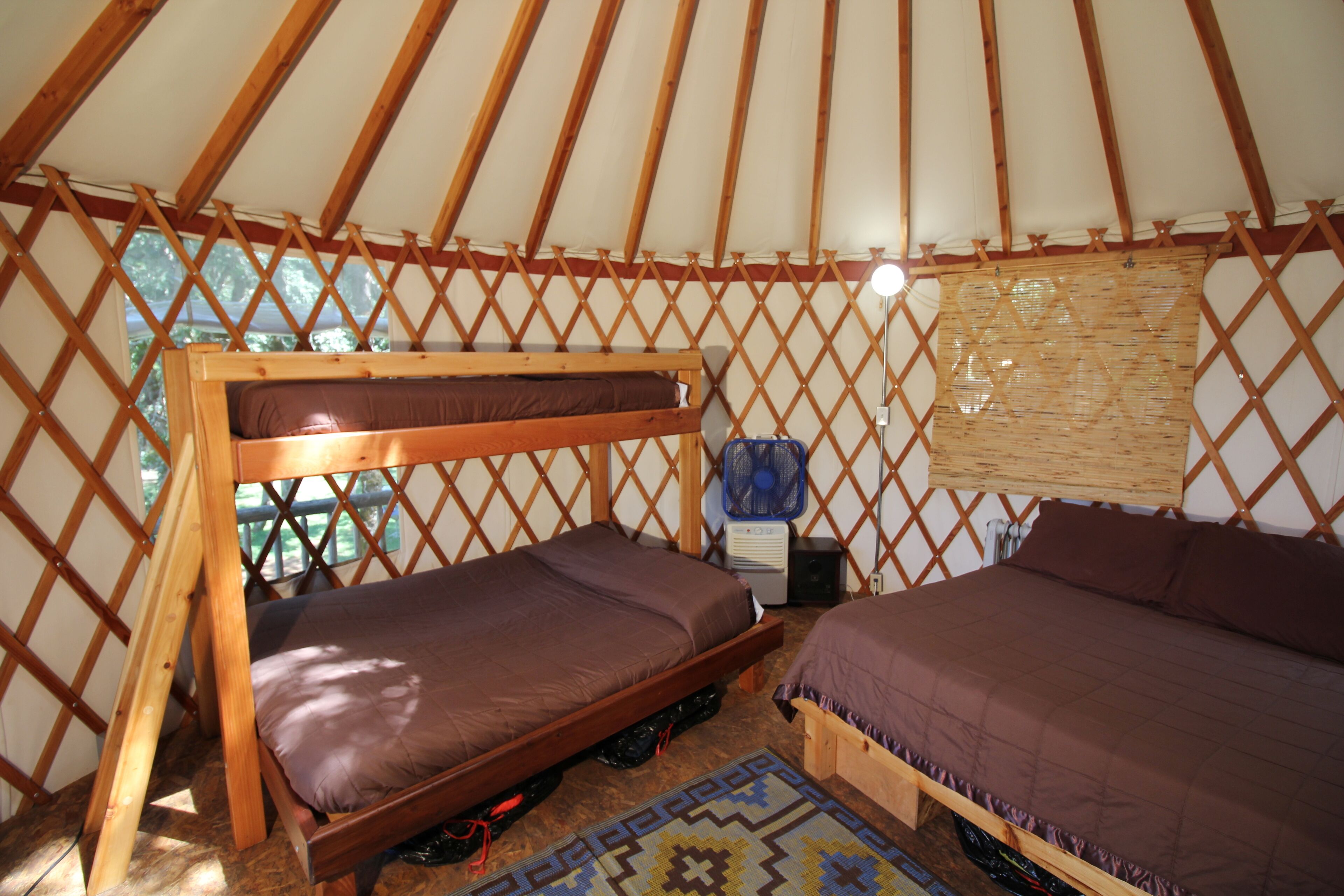 Una yurta con dos camas de madera, un ventilador y una mesita.