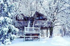 Une cabane en bois dotée d’un balcon, entourée d’arbres couverts de neige.