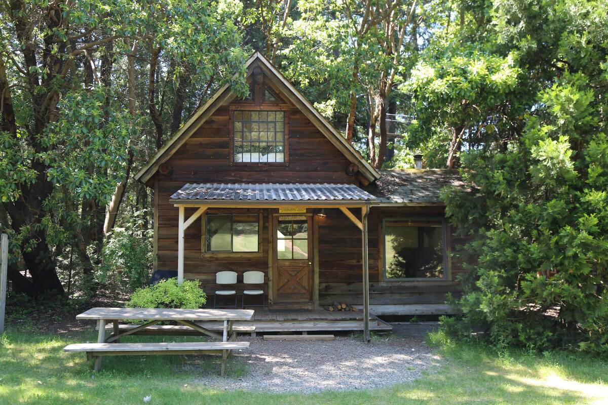 En træhytte med veranda, et picnicbord og et lille haveområde.
