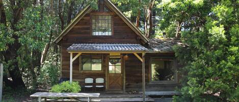 Une cabane en bois avec une véranda, une table de pique-nique et un petit coin jardin.
