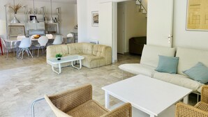 A modern living room with a sofa, coffee table, wicker chairs, and a dining area with chairs and a table.