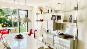 A modern kitchen with a dining table, chairs, pendant lights, and built-in shelves with kitchenware.