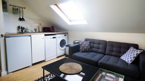 A compact living space with a kitchenette, a sofa, and a coffee table. - Le Cocon Urbain" 2-room apartment (Neuilly-Plaisance)