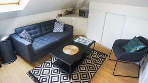 A compact living space with a sofa, a small coffee table, a chair, and a kitchenette area. - Le Cocon Urbain" 2-room apartment (Neuilly-Plaisance)