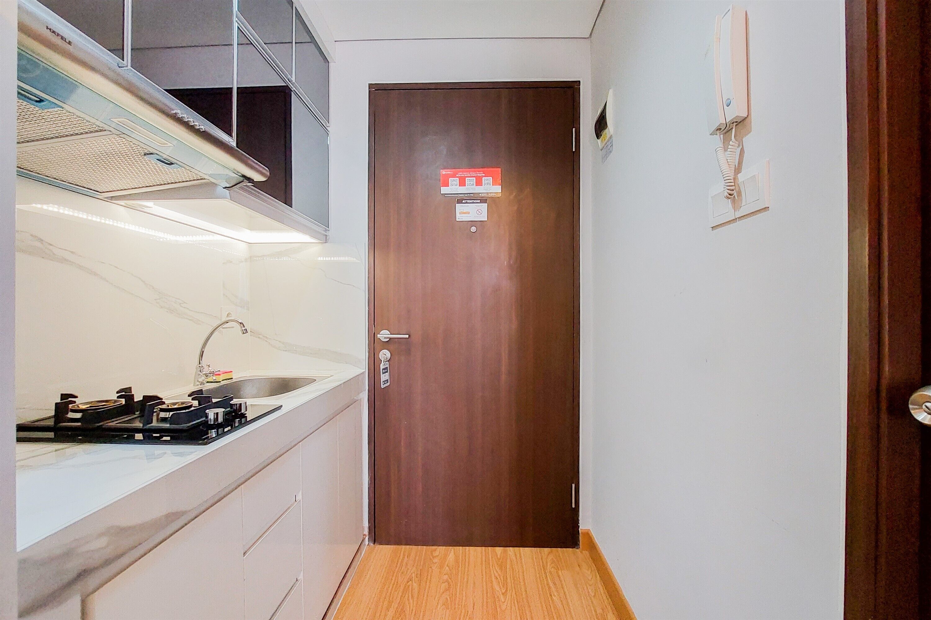 A narrow hallway with a wooden door, a kitchen area with a sink and stove, and a wall-mounted phone.