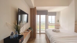 Una camera da letto con un letto, una televisione a parete, un balcone con vista e una scrivania in legno con una pianta e una bottiglia.