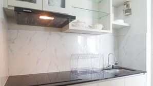 A kitchen with white cabinets, a black countertop, a stainless steel sink, and a glass shelf. - Exquisite And Vibrant 2Br Apartment At Taman Melati Surabaya (Surabaya)