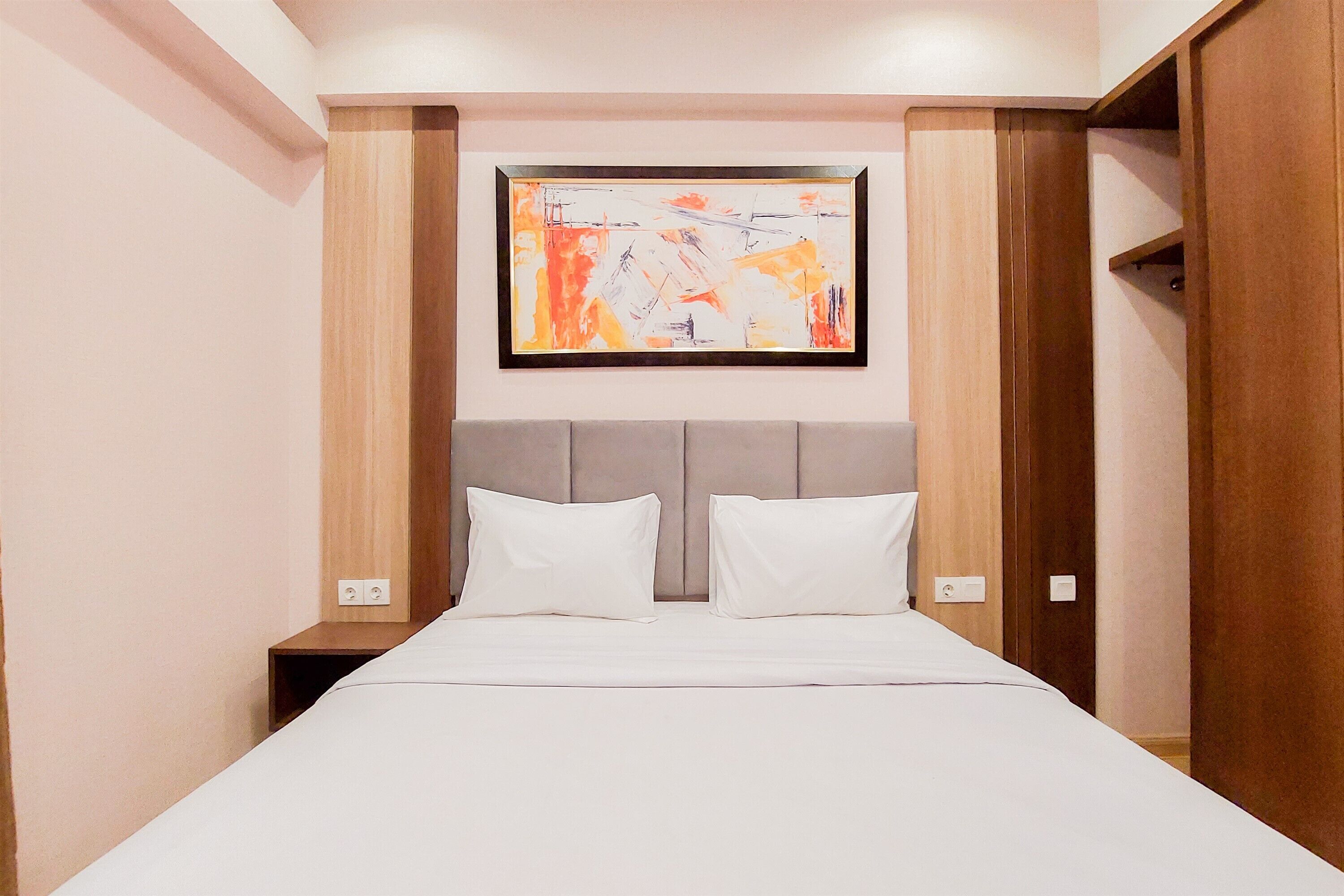 A hotel room with a bed, two pillows, a headboard, a nightstand, and a framed abstract painting on the wall.