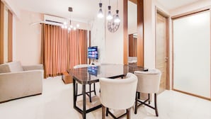 A modern dining area with a glass table, two white chairs, and a television on a stand. - Modern And Nice 2Br At 30Th Floor Sky House Bsd Apartment (Pagedangan)