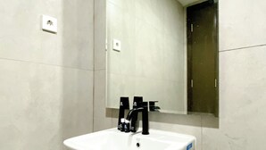 Un baño con lavamanos blanco, grifo negro y un espejo encima.