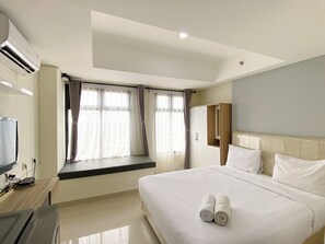 A hotel room with a bed, a TV, a window with curtains, and a wardrobe. - Full Furnished And Homey Studio Pollux Chadstone Apartment (Cikarang)