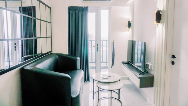 A modern living room with a black sofa, a small round table, a flat-screen TV, and a large mirror on the wall.