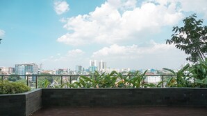 En tagterrasse med udsigt over byens skyline, en stenvæg og grønne planter.