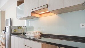 Et moderne køkken med et rustfrit stål køleskab, hvide skabe, en sort bordplade og en indbygget ovn.