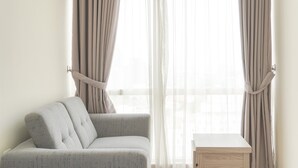 Et værelse med en grå polstret sofa, et lille træsidebord og lette gardiner.