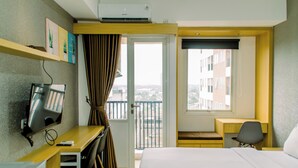 A hotel room with a bed, a desk with a chair, a TV, a window with a view of buildings, and an air conditioning unit. - Nice Studio Apartment At Urban Height Residence (South Tangerang)