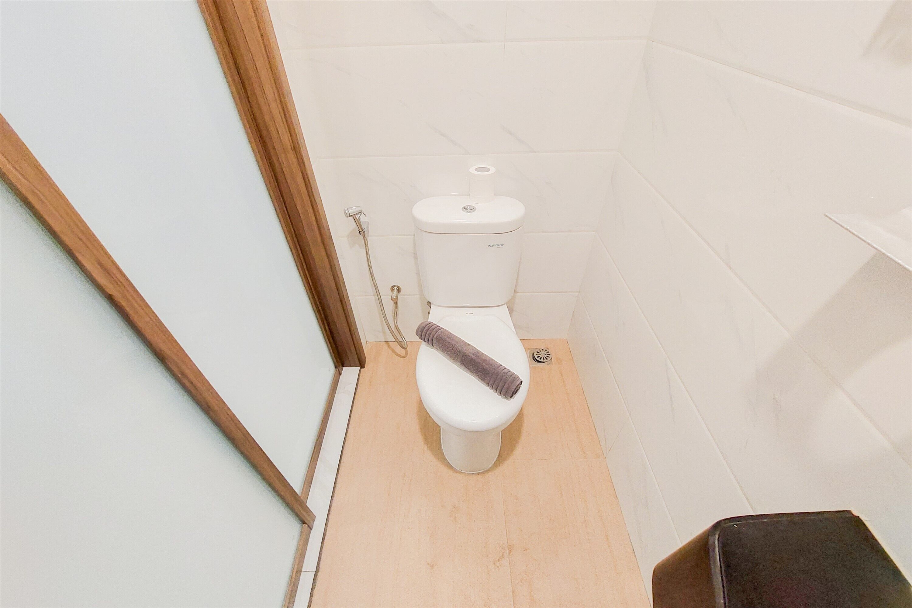 A small, compact bathroom with a toilet, a wooden floor, and a white tiled wall.
