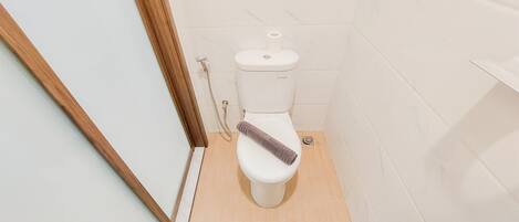 A small, compact bathroom with a toilet, a wooden floor, and a white tiled wall.