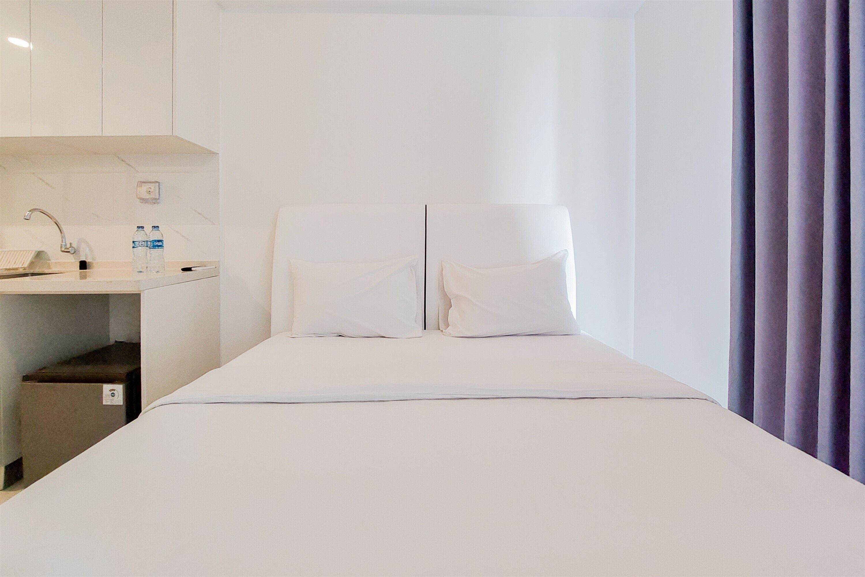 A hotel room with a bed, a bedside table, a sink, and a mirror.