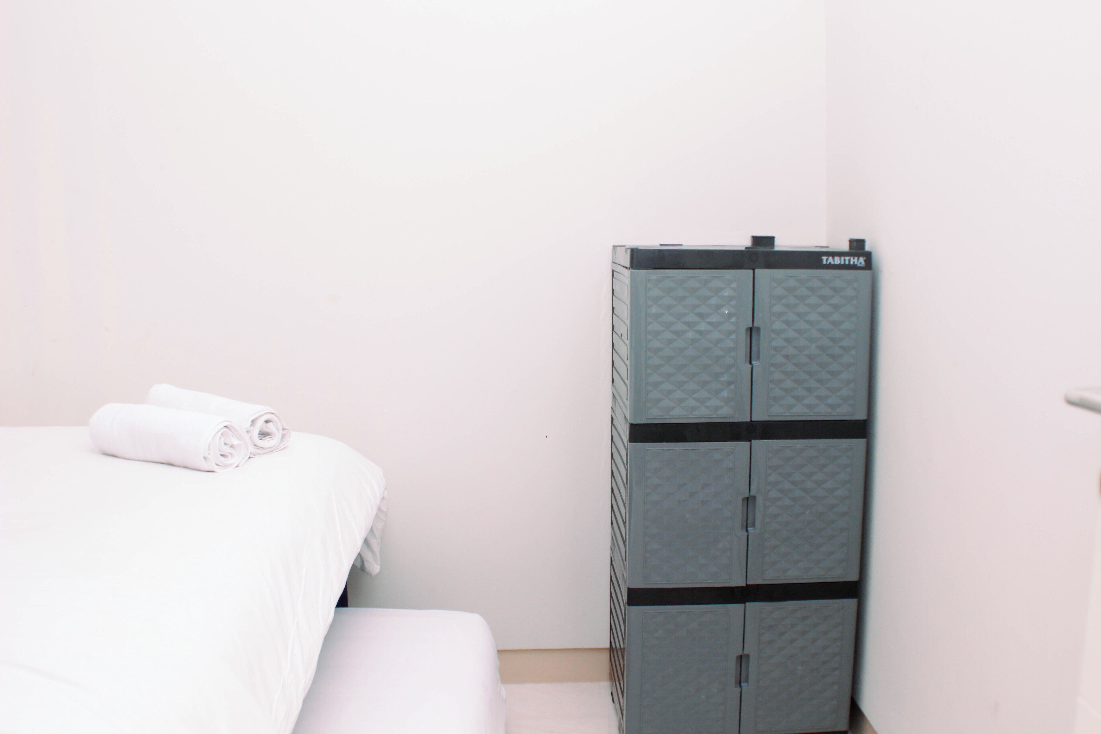 A hotel room with a bed, a wardrobe, and a rolled-up towel on the bed.