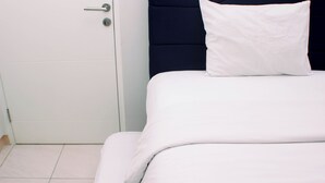 Ett hotellrum med en säng, en vit dörr och en mörk sänggavel.
