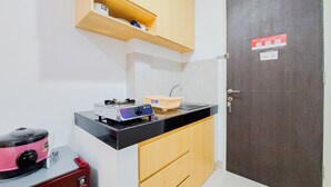 A compact kitchen with a black countertop, wooden cabinets, a sink, and a stove. - Homey And Enjoy Living Studio Serpong Garden Apartment (Cisauk)