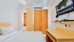 A hotel room with a bed, a wooden desk, a television mounted on the wall, and a curtain divider. - Homey And Enjoy Living Studio Serpong Garden Apartment (Cisauk)