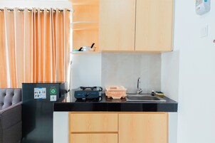 Una kitchenette compacta con encimera negra, estufa integrada, lavamanos y muebles de madera.