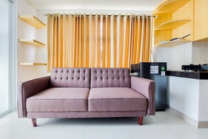 Una sala de estar moderna con un sofá, un área de cocina con electrodomésticos y una cortina.