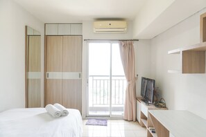 A hotel room with a bed, a TV, a wardrobe, and a balcony. - Modern Look And Homey Studio Serpong Greenview Apartment (South Tangerang)