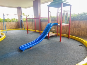 Un'area giochi con uno scivolo blu, bordi di sicurezza rossi e gialli e una zona giochi coperta.