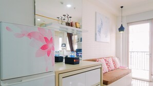 A modern living room with a sofa, a coffee table, and a refrigerator. There is a window with blinds and a ceiling light. - Best Choice And Restful Studio Signature Park Grande Apartment (Jakarta)