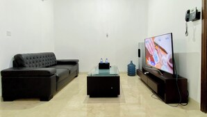 Een woonkamer met een zwarte bank, een glazen salontafel, een tv op een houten standaard en een waterdispenser.