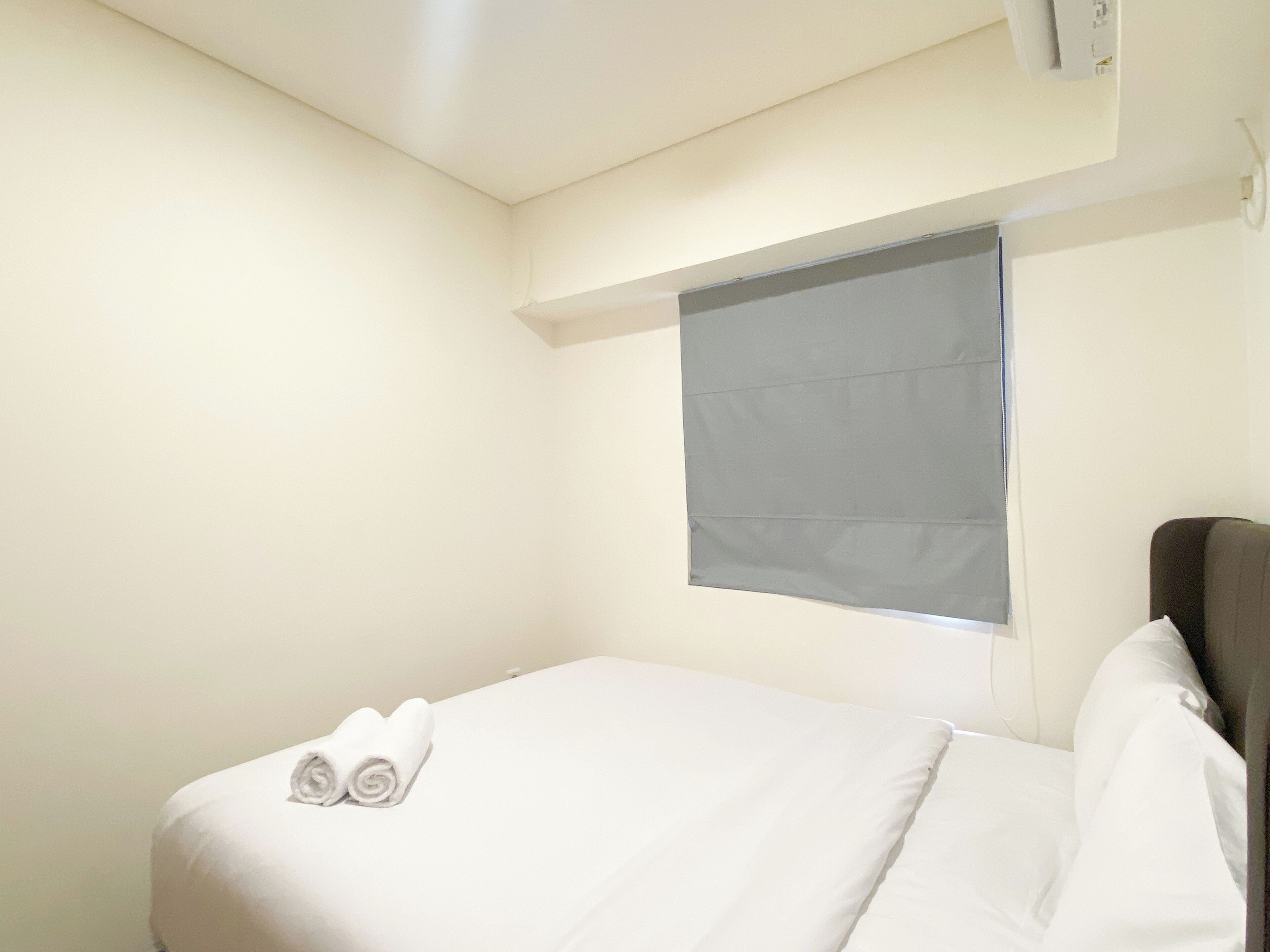 A small, neatly made bed with white linens and two rolled towels placed at the foot.