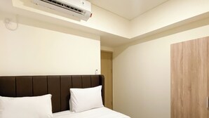 A hotel room with a bed, a wooden wardrobe, and an air conditioning unit. - Good Deal And Comfortable 2Br Meikarta Apartment (Cikarang)