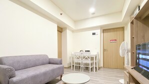 A modern living room with a grey sofa, a small round table, and a TV on a wooden stand. - Good Deal And Comfortable 2Br Meikarta Apartment (Cikarang)